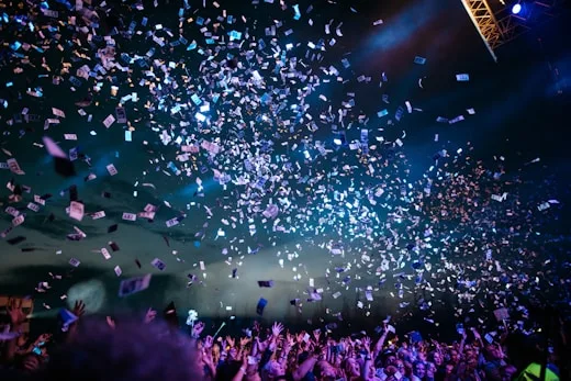 A large crowd enjoys a concert with confetti falling, showcasing creative arts events.