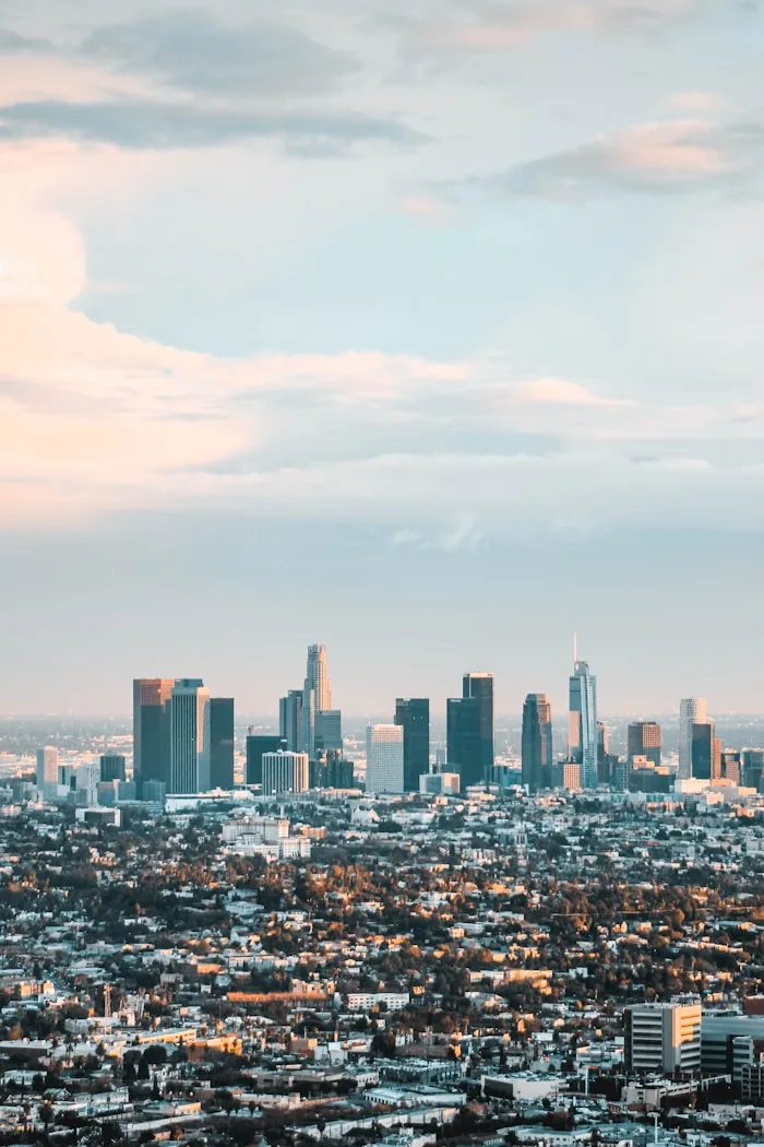 The Los Angeles skyline and urban landscape are visible under cloudy skies.