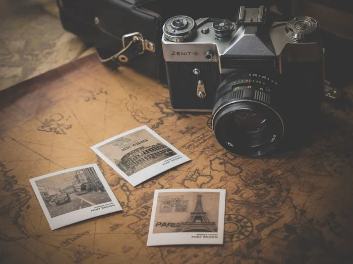 A vintage Zenit-E camera sits on a map covered in travel photos, representing creative arts inspiration.